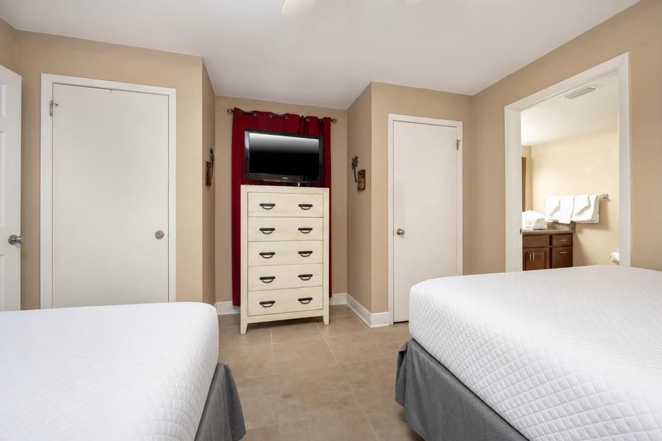 The guest bedroom features two queen beds, a dresser with TV, and an adjoining bathroom with fresh towels on the counter