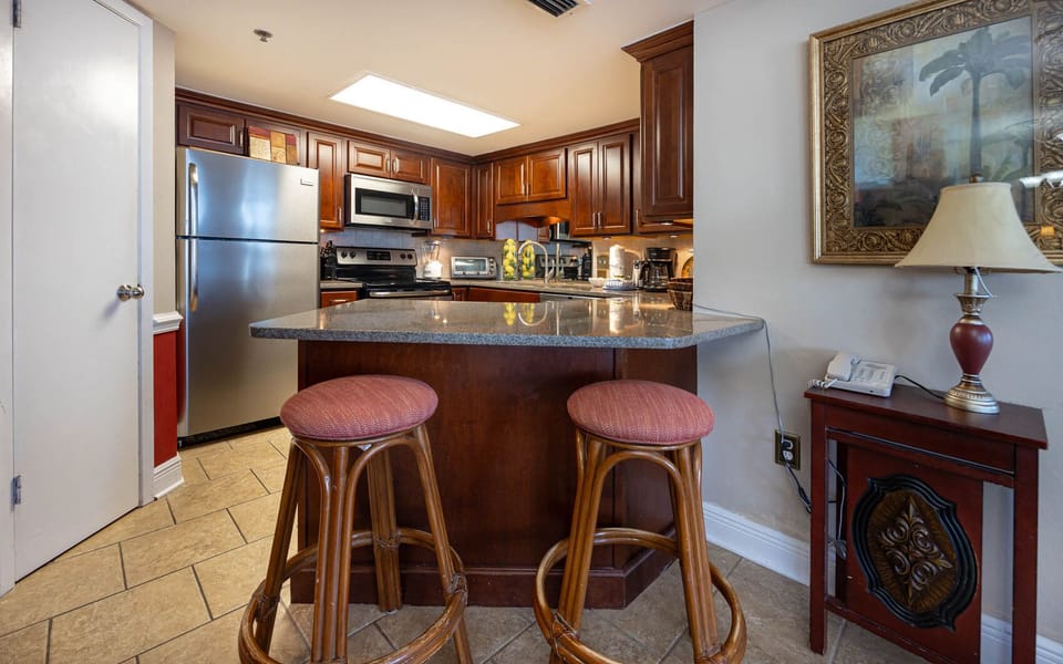 Rich wooden cabinetry complements the granite countertops in this modern kitchen with a breakfast bar and two stools