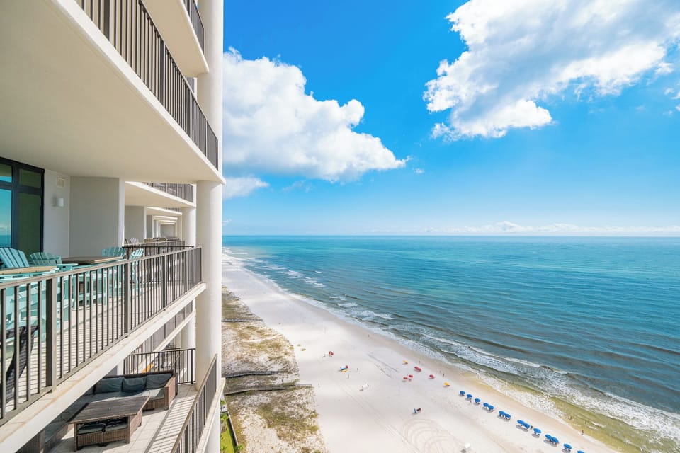 Panoramic views from the balcony showcase the pristine beach and vibrant umbrellas against a clear blue sky