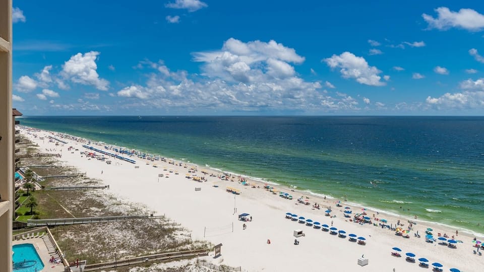 A vibrant beach scene features colorful umbrellas and sunbathers enjoying the white sand under a bright blue sky