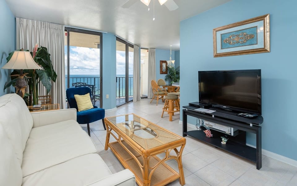 Bright living area featuring a white sofa with queen sleeper, blue chair, and a view of the beach through balcony doors