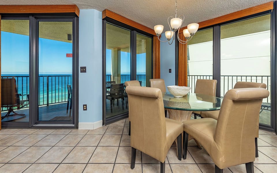 A glass dining table with beige chairs offers a perfect spot to enjoy meals while overlooking the tranquil beachfront