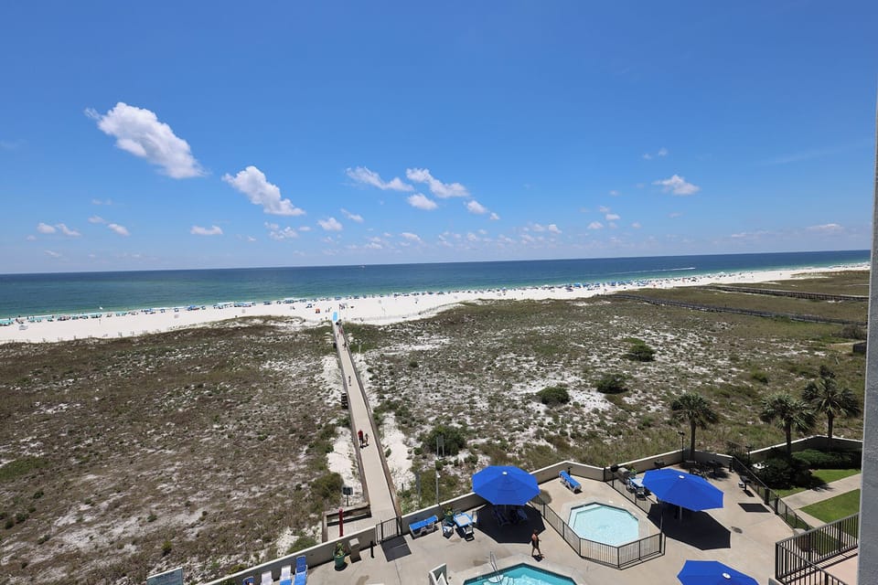 Stunning view of the beach and turquoise gulf waters, featuring a path leading to the shore and a pool area below