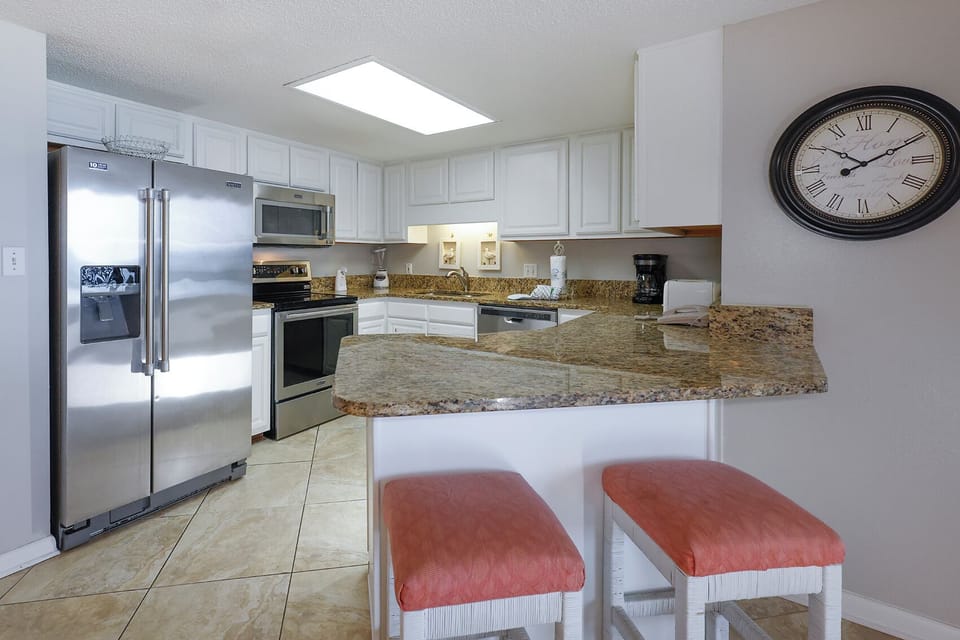 Bright kitchen area features granite countertops, modern appliances, and a breakfast bar with coral-colored stools