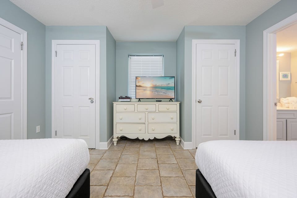 Bright guest bedroom featuring two double beds, a dresser with a TV, and coastal decor, creating a relaxed atmosphere