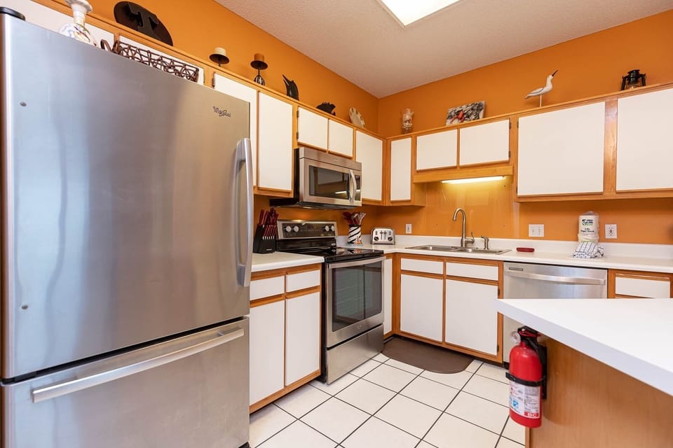 Bright kitchen features white cabinetry, stainless appliances, and a cozy atmosphere enhanced by warm orange walls