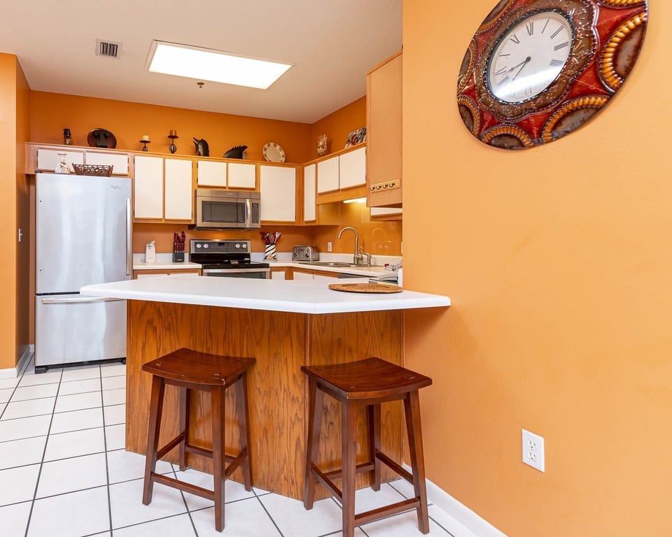 Bright orange walls complement the wood accents in this modern kitchen area featuring a breakfast bar with two stools