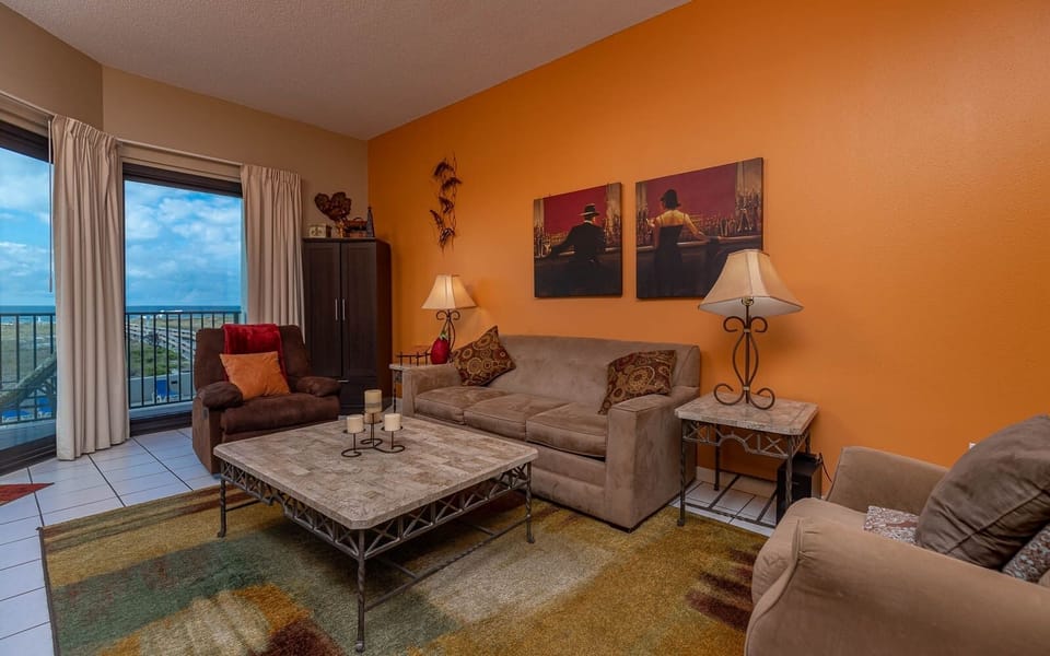 Living area features a plush sofa with queen sleeper, a coffee table, and vibrant orange walls enhancing the ambiance