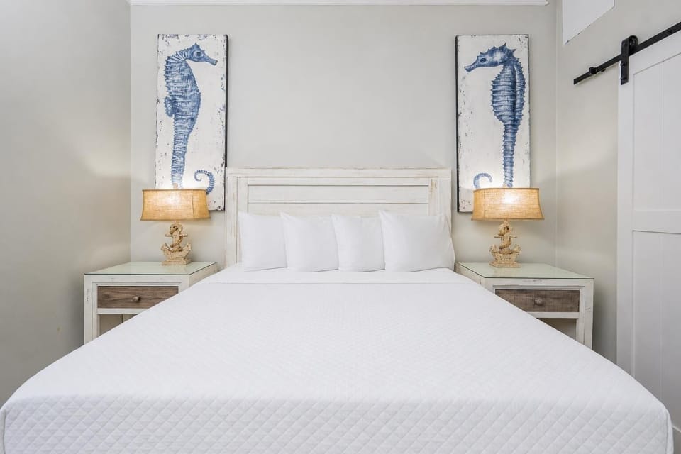 This guest bedroom features a queen bed, nautical decor with seahorse artwork, and warm lighting for a relaxing atmosphere