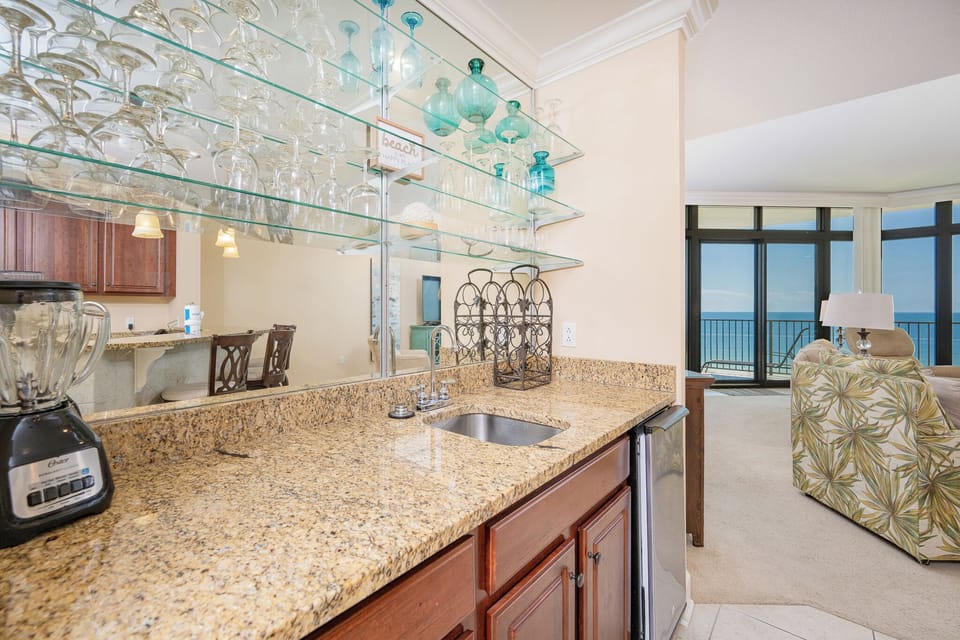 Wet bar with granite countertops, a blender, and a view of the tranquil coastline through large windows
