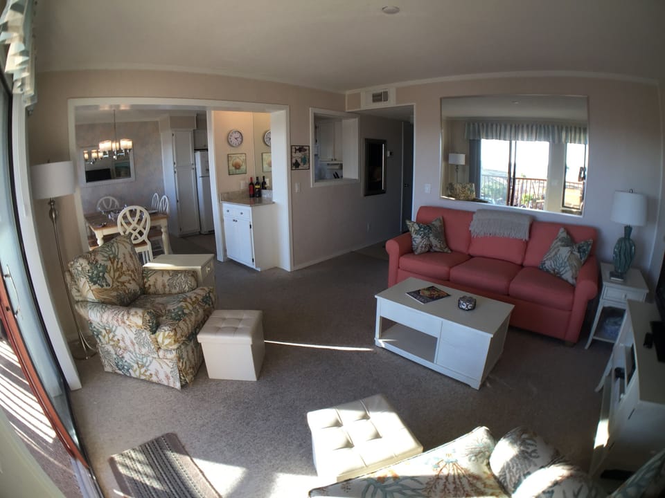 Wide angle view of the living room, dining room, large reflective mirror.