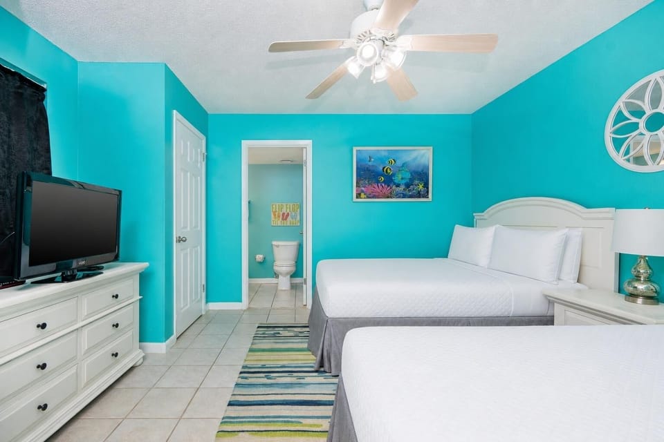 Bright cheerful walls complement two double beds in this guest room, featuring a TV and a vibrant area rug for a fun vibe