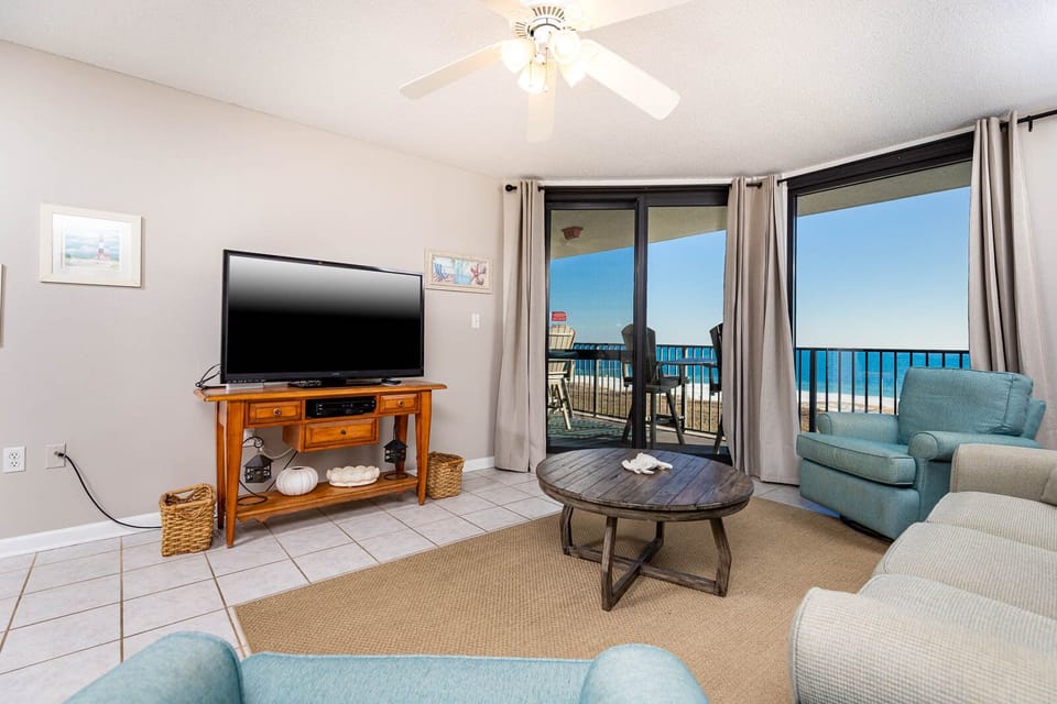 Cozy living area features a TV, comfortable seating, and sliding glass doors opening to a balcony with a view of the gulf