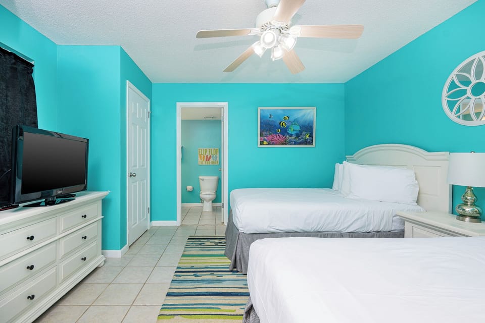 Bright cheerful walls complement two double beds in this guest room, featuring a TV and a vibrant area rug for a fun vibe