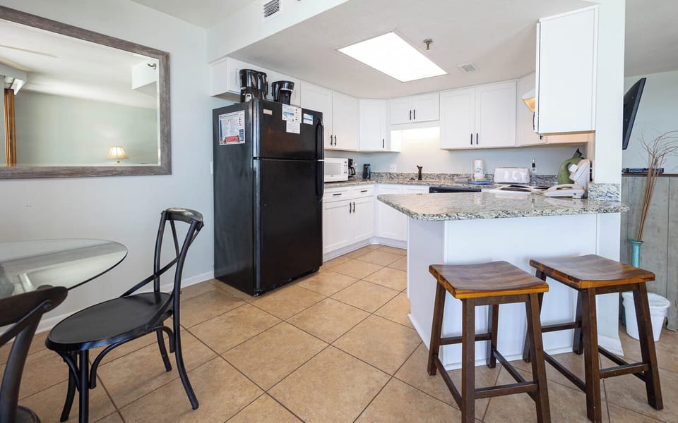 Bright kitchen featuring white cabinetry, granite countertops, a black refrigerator, and the dining area with a glass table