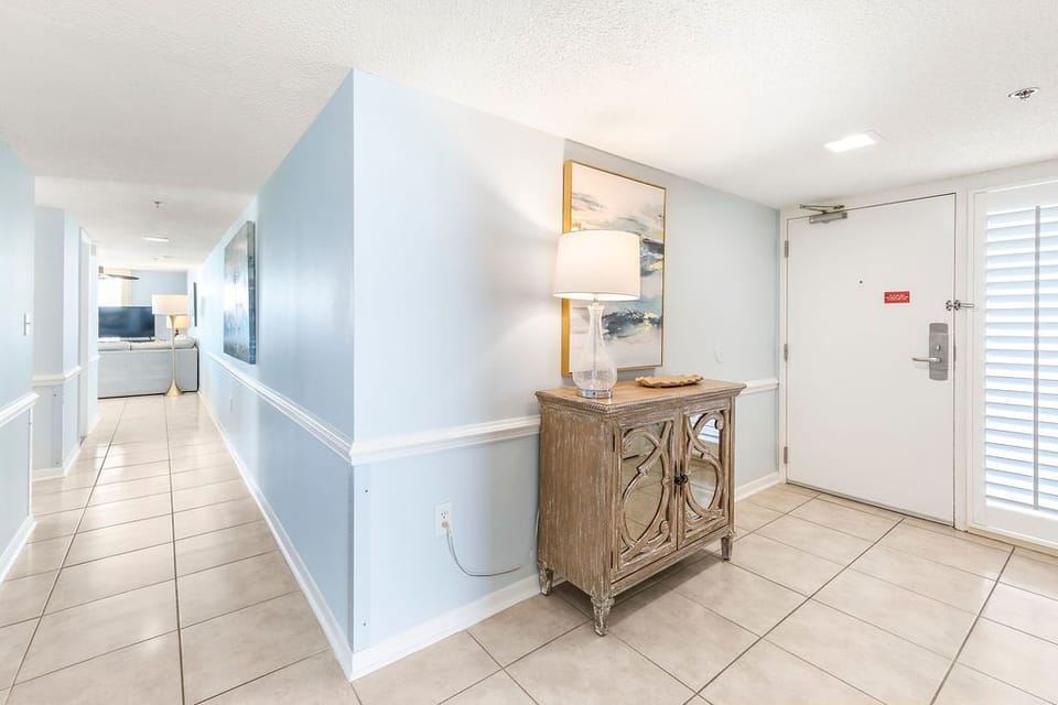 As you enter, your feet meet cool tile while soft light glows from a glass lamp on rustic wood
