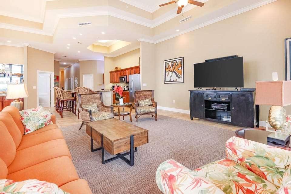 This inviting living area features an orange sofa, tropical accents, and a large TV, perfect for relaxation and entertainment