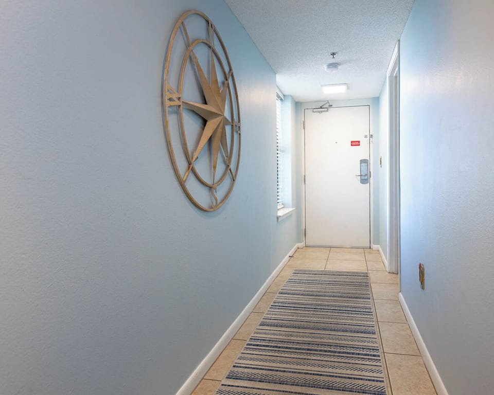 Welcoming entryway features light blue walls, a decorative compass wall art piece, and a striped runner leading to the door