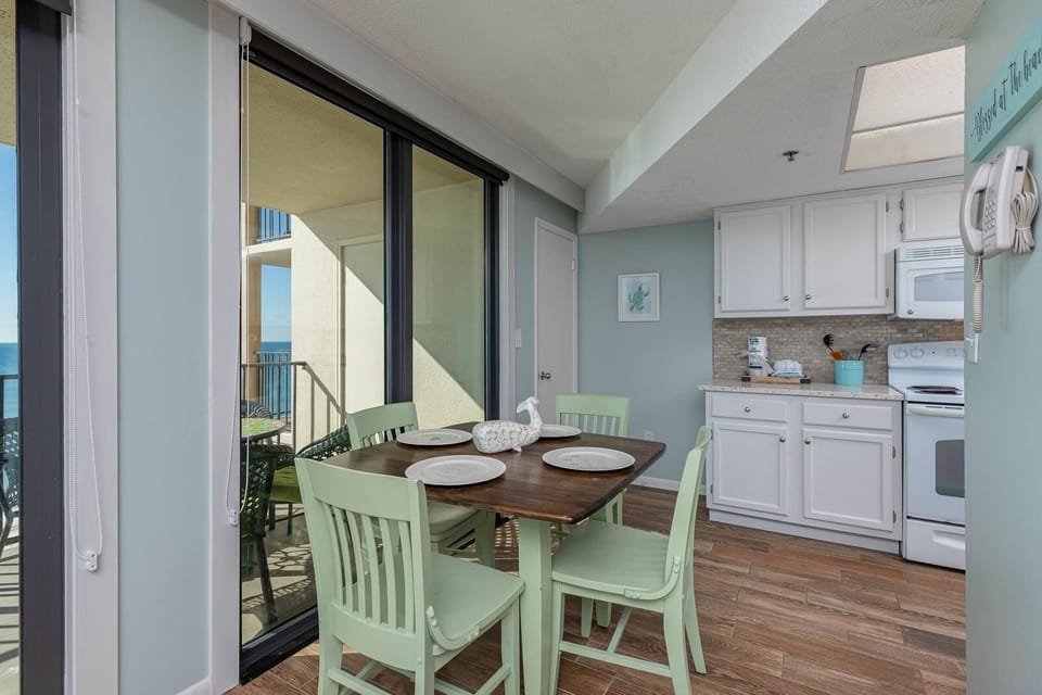 This dining area features a charming table with pastel chairs, a view of the beach, and a modern kitchen with white cabinetry