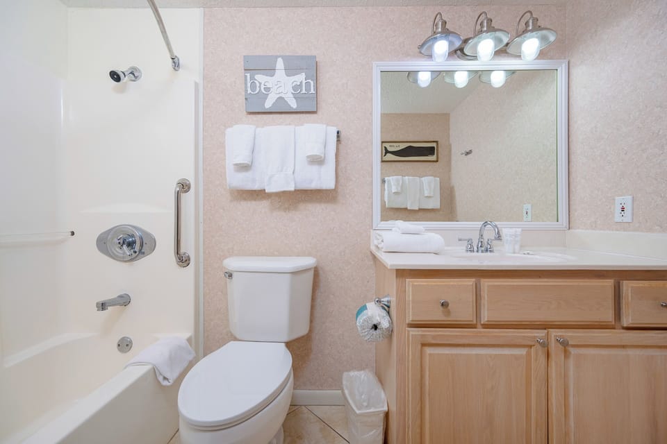 The full bath features a tub/shower combo, light wood cabinetry, and beach decor for a refreshing retreat