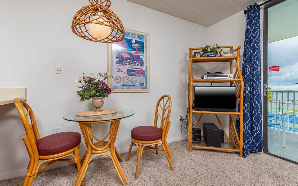 This cozy dining area features a glass table, wicker chairs, and a TV, with a lovely view of the lagoon outside