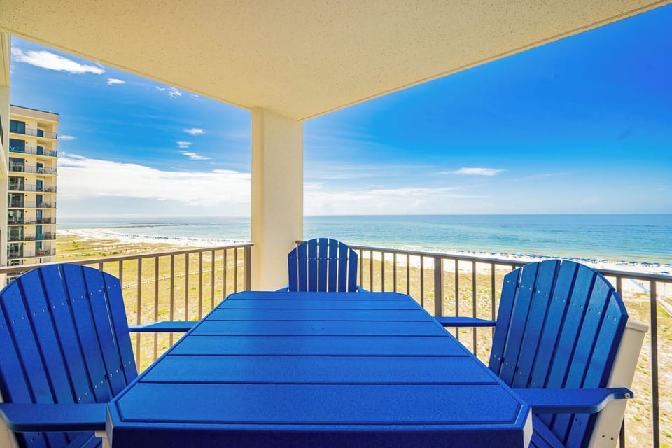 Bright blue chairs surround a table on the balcony, offering a view of the beach and the inviting gulf waters