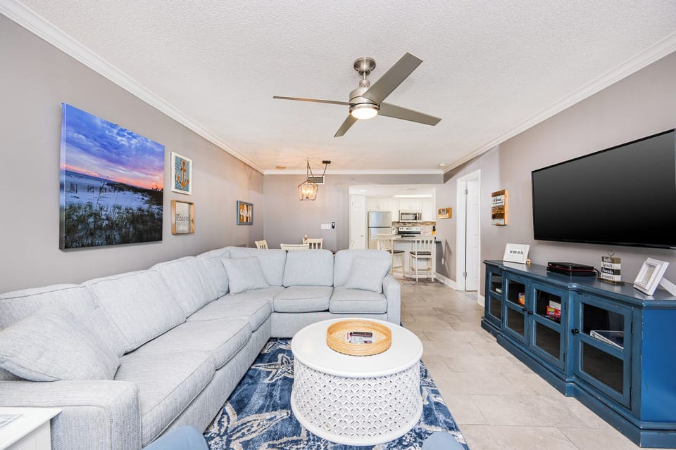 Cozy living area features a large sectional sofa, a TV, and a decorative coffee table, with views leading to the kitchen