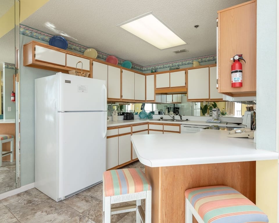 Bright and functional kitchen area features white cabinetry, a breakfast bar with colorful stools, and ample counter space