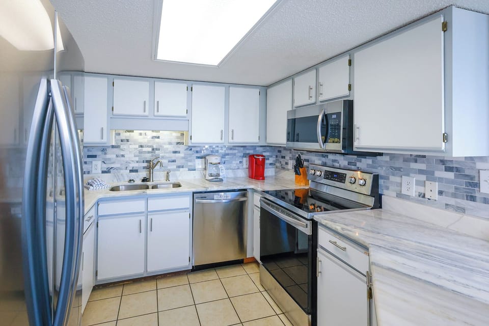 Kitchen featuring sleek cabinetry, a marbled countertop, and a breakfast bar with a Keurig, coffee maker, and red accents