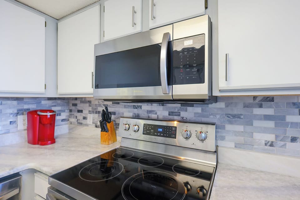 Modern kitchen features sleek cabinetry, marbled countertop, Keurig, and coffee maker, perfect for preparing meals and drinks