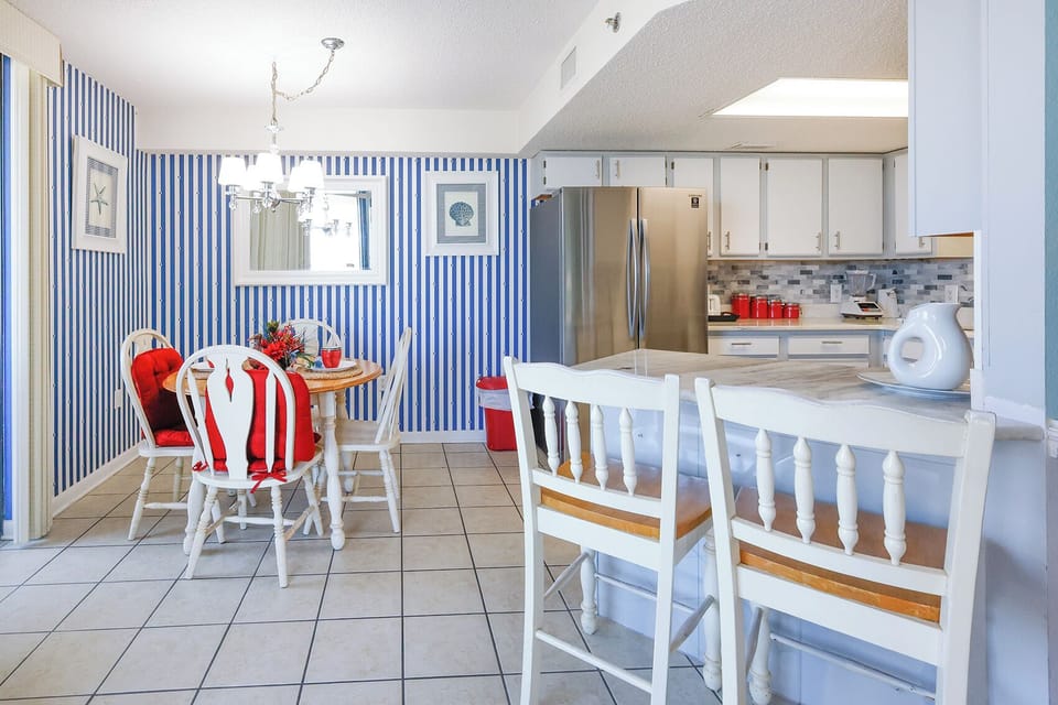 Dining area featuring a round table with red accents, surrounded by white chairs, leading into a well-equipped modern kitchen
