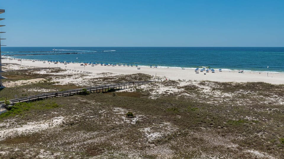 Expansive view of the beach with white sand, colorful umbrellas, and gentle waves, creating a serene coastal atmosphere