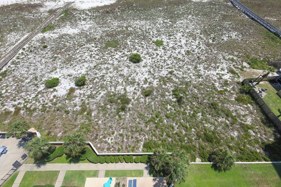 Lush greenery and white sand stretch across the landscape, leading to a serene beach access path framed by palm trees