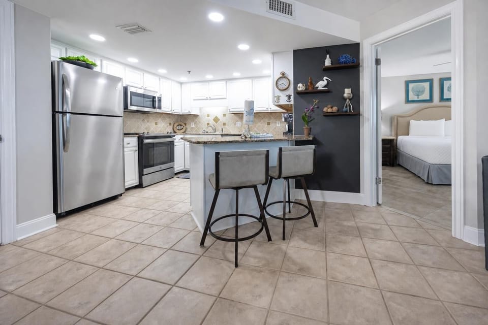 Modern kitchen features a breakfast bar with two stools, stainless appliances, and granite countertops