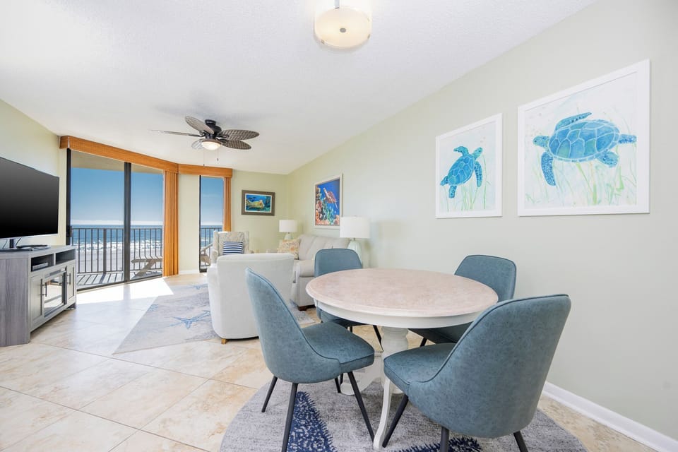 Living area features a cozy seating arrangement, a round dining table, and expansive glass doors revealing beach front views