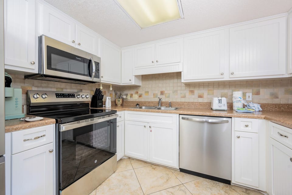 White cabinetry complements the kitchen's sleek appliances and textured tile backsplash, creating an inviting cooking space