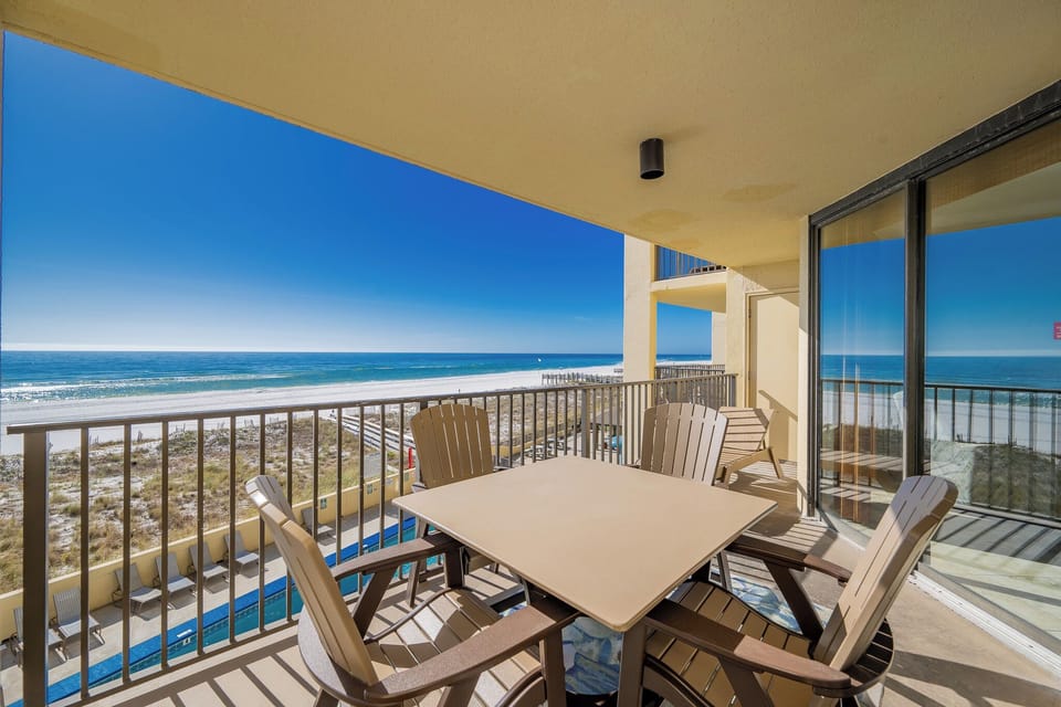 A spacious balcony features a table and chairs, offering a direct view of the tranquil beachfront and glistening waters