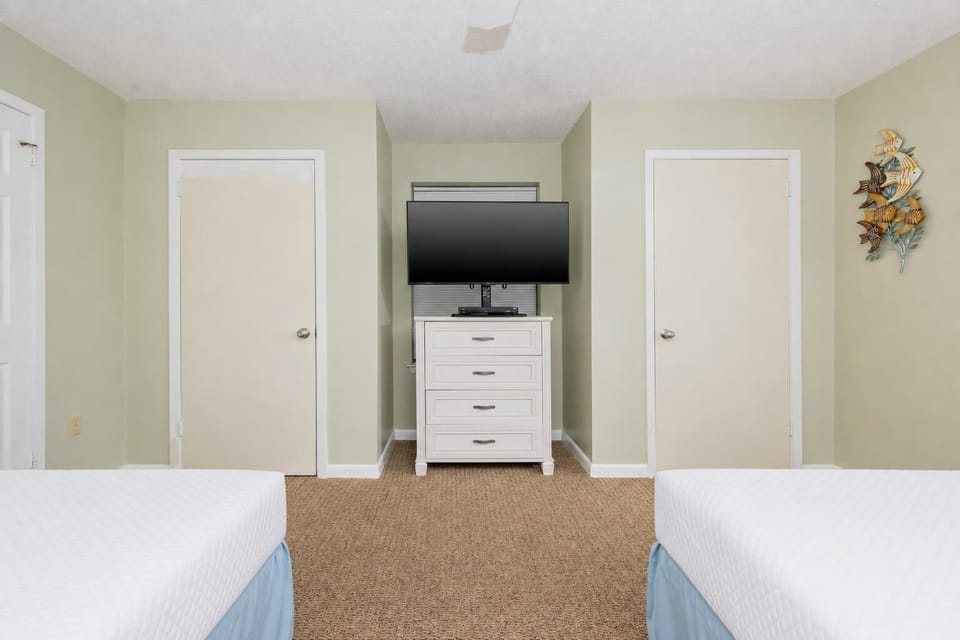 Brightly colored walls frame a cozy guest room featuring two full beds, a dresser, and a wall-mounted TV for entertainment