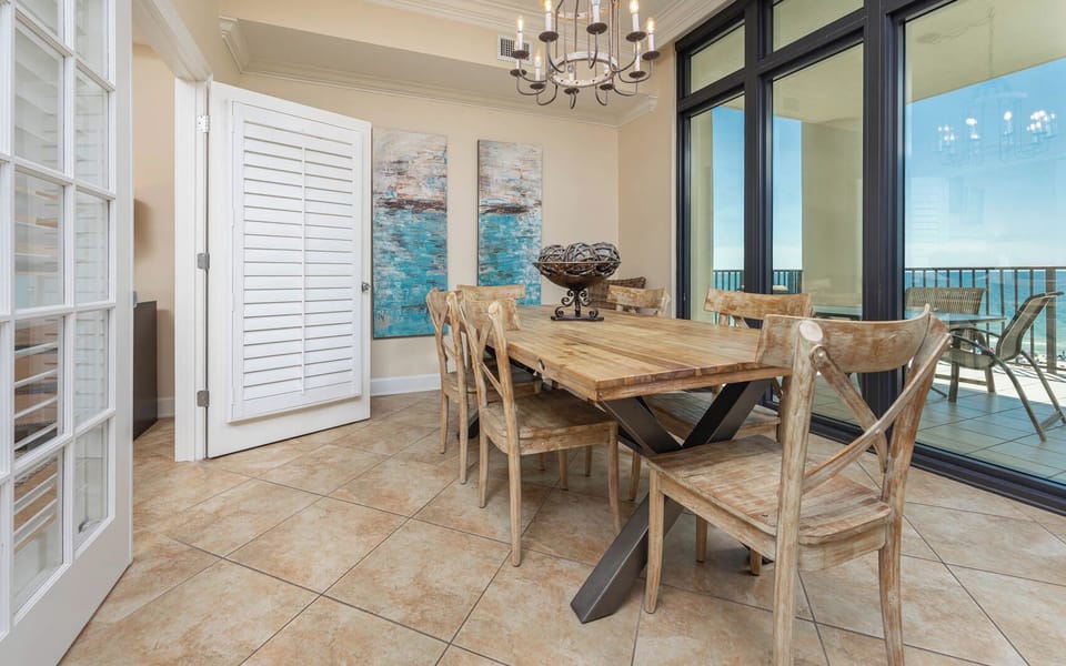 Dining area featuring a rustic wooden table, stylish chairs, and large windows showcasing a beautiful coastal view