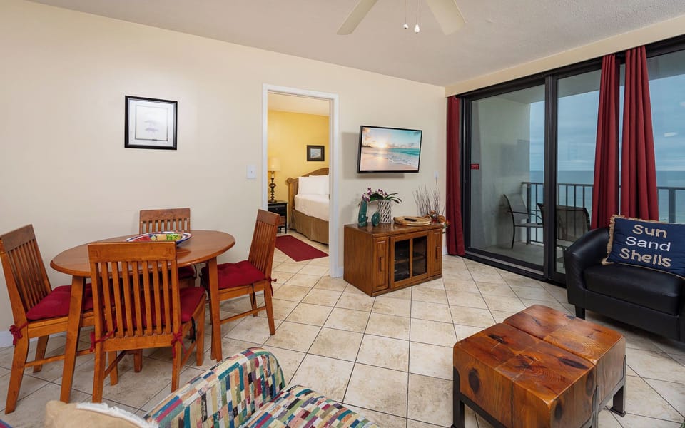 Cozy living area featuring a dining table, colorful couch with queen sleeper, and a view of the beach through balcony doors
