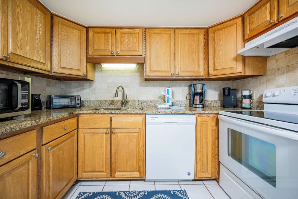 The kitchen features wooden cabinetry, granite countertops, and essential appliances, including a coffee station