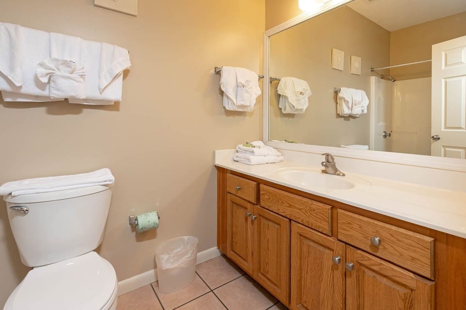 The wooden cabinetry complements the spacious vanity area, featuring neatly arranged towels and a tub/shower combo