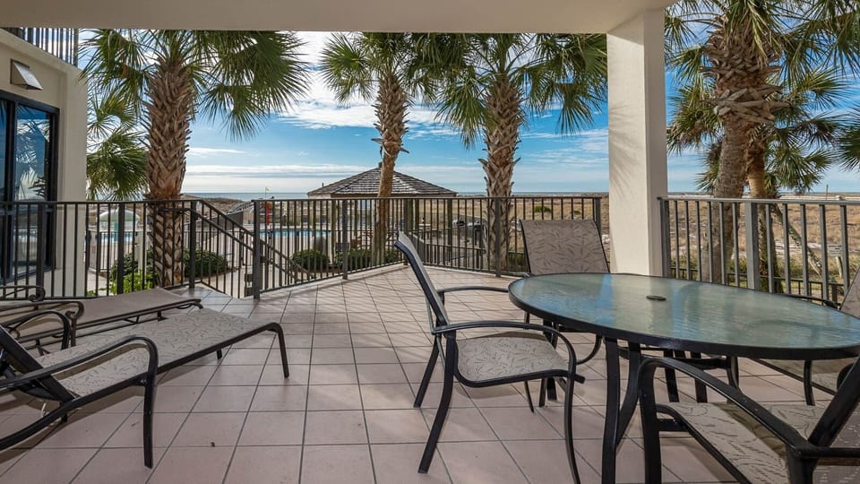 Relax on the spacious patio surrounded by palm trees, offering views of the pool area and the tranquil beach beyond
