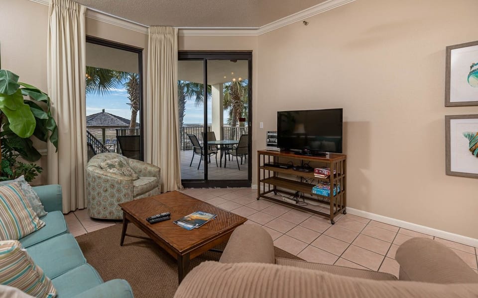 Living area features a comfortable sofa with queen sleeper, accent chair, and a view of the balcony overlooking the beach
