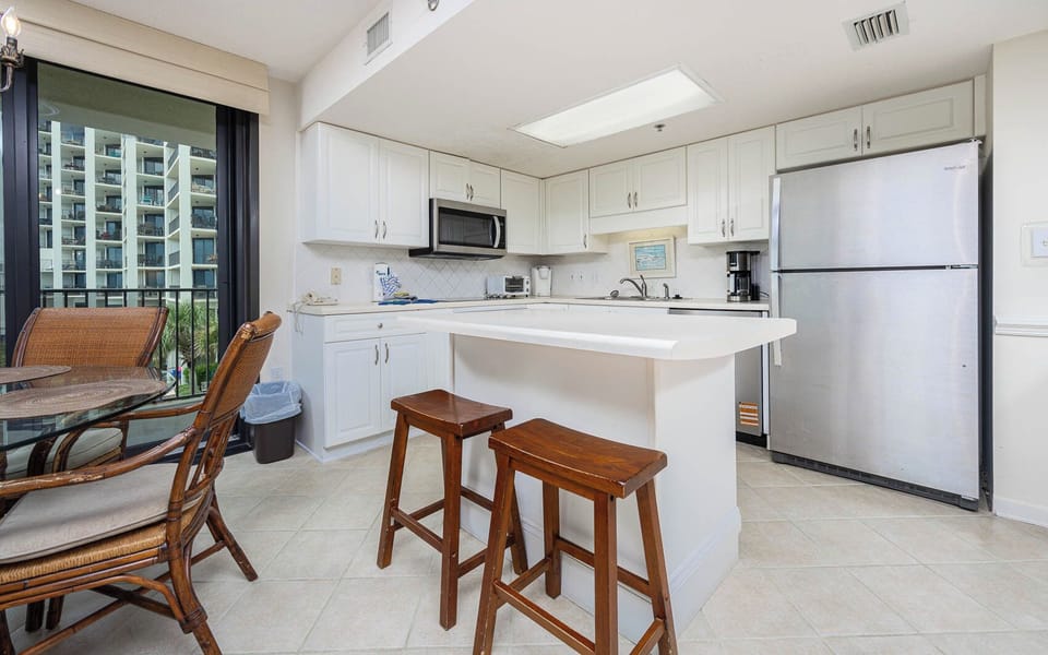 Bright kitchen area features white cabinetry, a breakfast bar with wooden stools, and a view of the beach