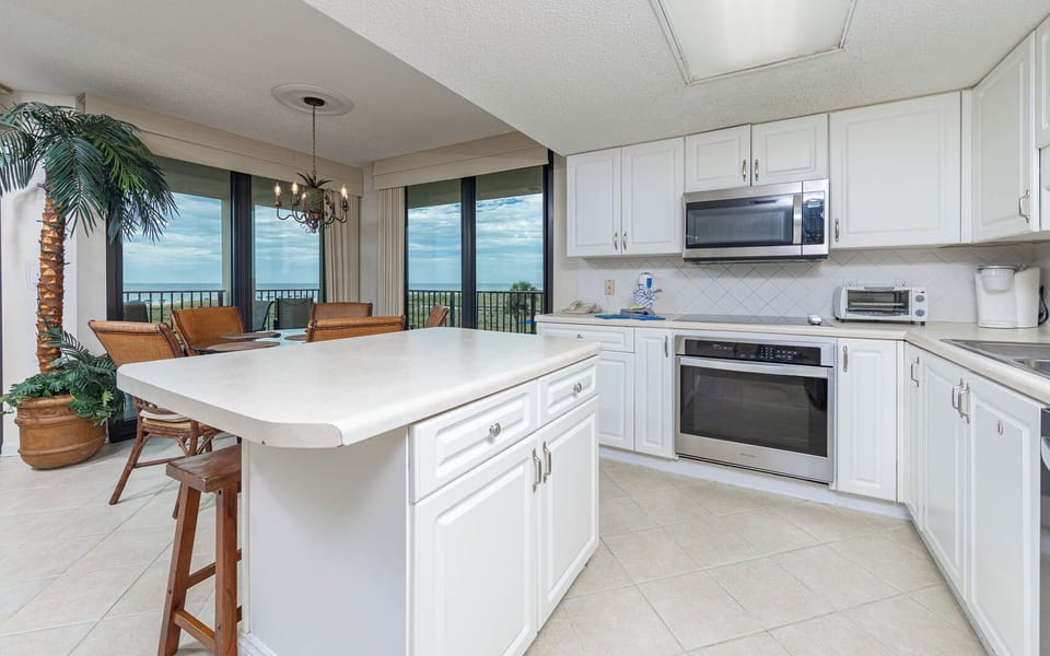 Bright white cabinetry complements this modern kitchen, featuring a breakfast bar and a stunning view of the beach