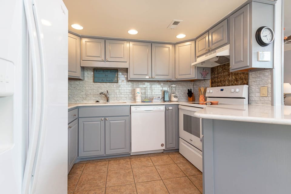 Kitchen featuring light gray cabinetry, white appliances, and a charming beach wall sign