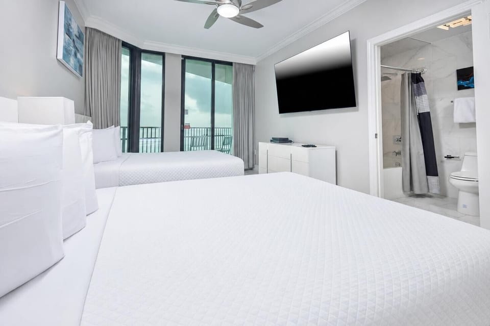 Unwind in this guest bedroom with two comfortable queen beds, a large TV, and access to a balcony for fresh air