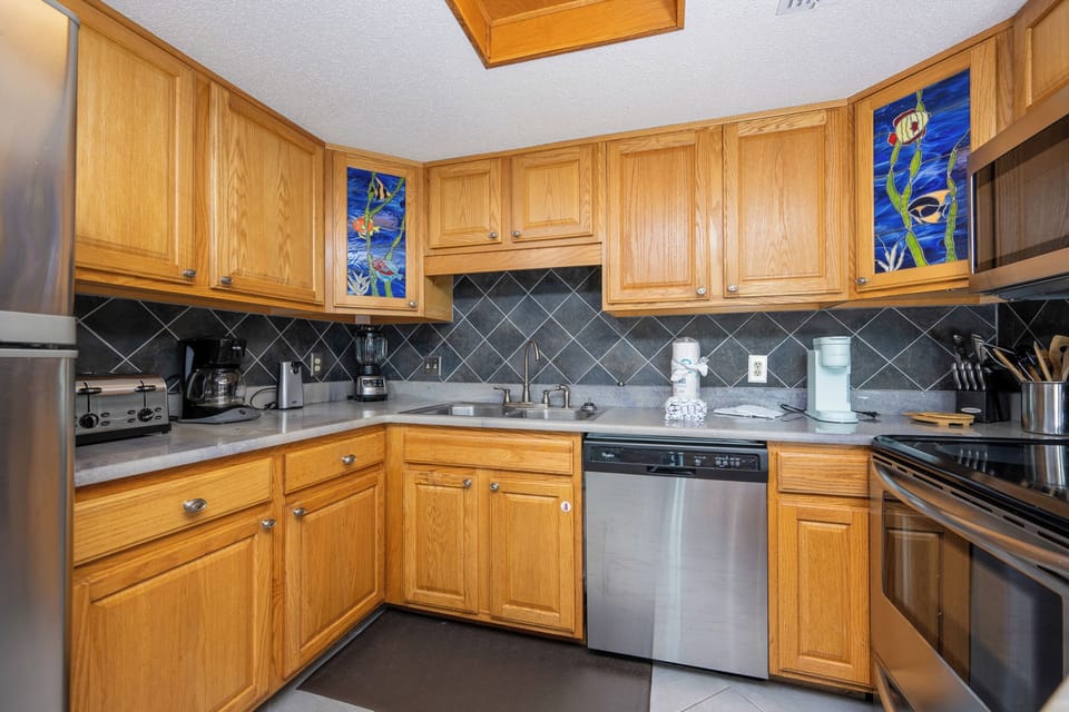 The kitchen features warm wood cabinetry, a sleek breakfast bar area, and colorful artwork, creating a vibrant cooking space