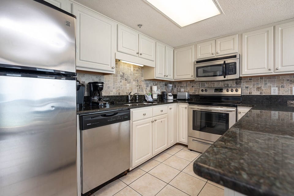 This kitchen features sleek stainless appliances, granite countertops, stylish tile backsplash, a Keurig and a coffee maker